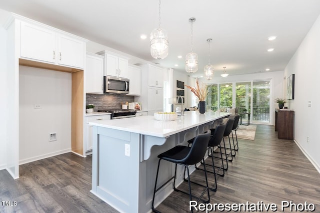 kitchen with white cabinetry, tasteful backsplash, decorative light fixtures, appliances with stainless steel finishes, and a kitchen island with sink