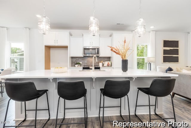 kitchen featuring backsplash, decorative light fixtures, a wealth of natural light, and a large island with sink