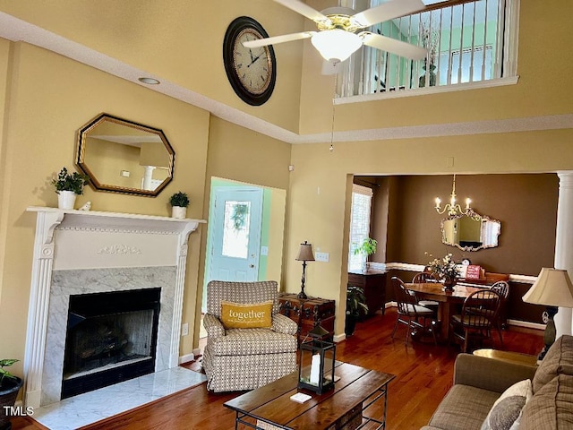 living room featuring ceiling fan with notable chandelier, a premium fireplace, wood finished floors, a towering ceiling, and baseboards