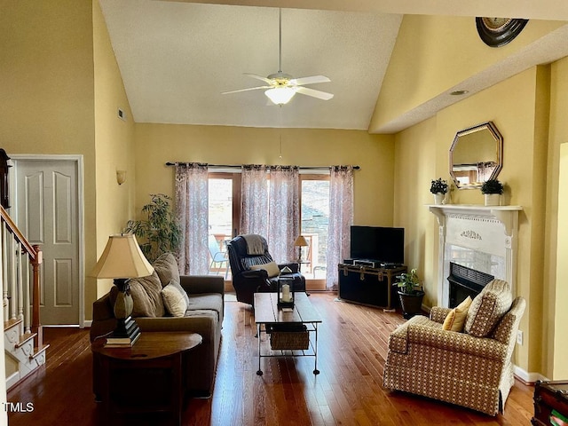 living area featuring stairs, high vaulted ceiling, a fireplace, and wood finished floors