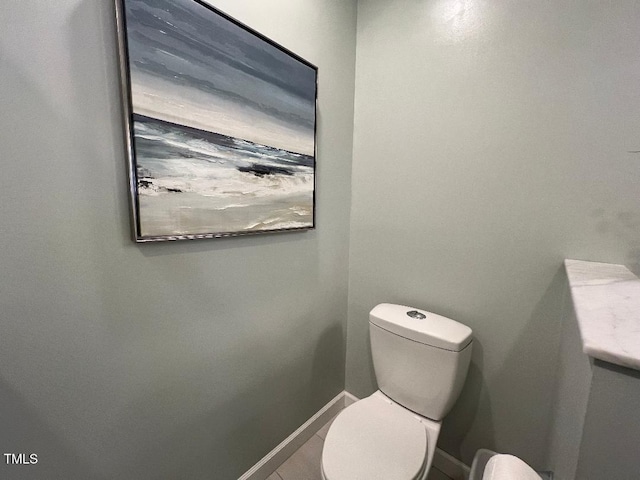 half bath featuring tile patterned flooring, toilet, and baseboards