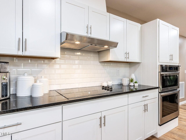 kitchen with double oven, tasteful backsplash, white cabinets, and under cabinet range hood