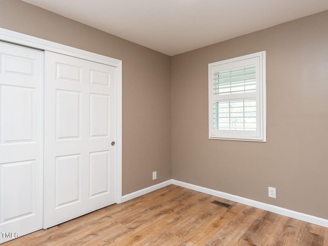 unfurnished bedroom with light wood-style floors, a closet, visible vents, and baseboards