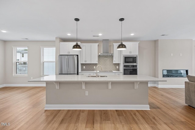 kitchen with white cabinetry, stainless steel appliances, sink, and wall chimney range hood