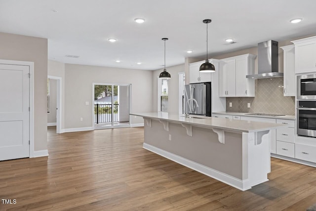 kitchen featuring a kitchen island with sink, wall chimney range hood, a breakfast bar area, and white cabinets