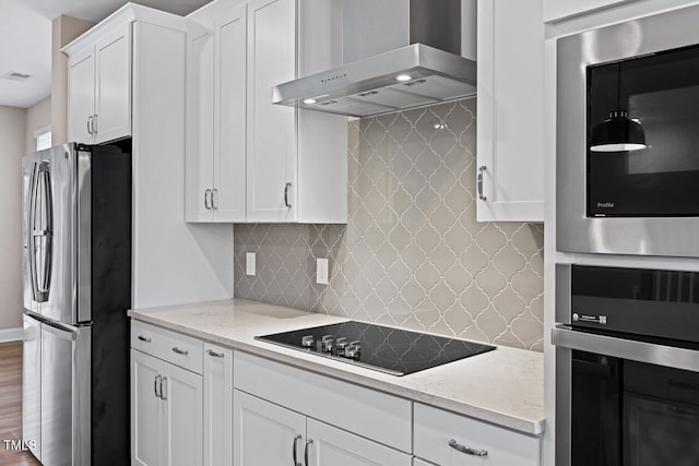 kitchen featuring stainless steel refrigerator, white cabinetry, black electric stovetop, light stone countertops, and wall chimney exhaust hood