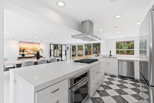 kitchen with a kitchen island, appliances with stainless steel finishes, island range hood, white cabinetry, and sink