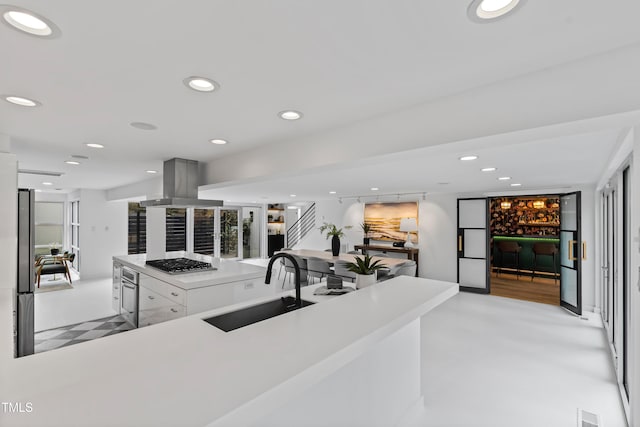 kitchen with appliances with stainless steel finishes, sink, island range hood, and white cabinets