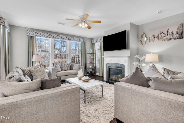 living room featuring dark wood-style floors, a high end fireplace, visible vents, and ceiling fan