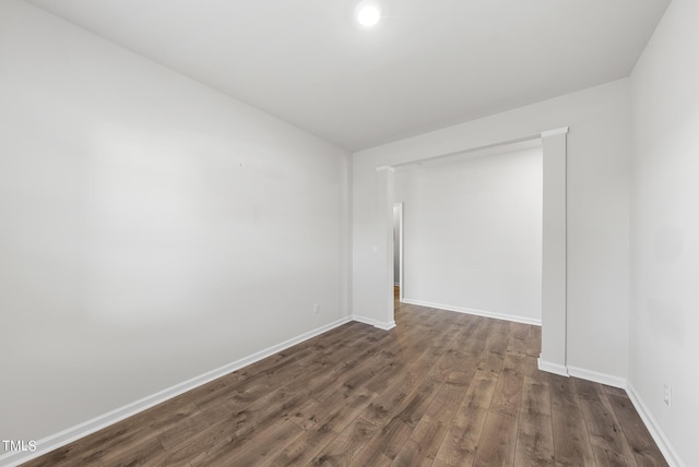 unfurnished room featuring baseboards and dark wood-type flooring