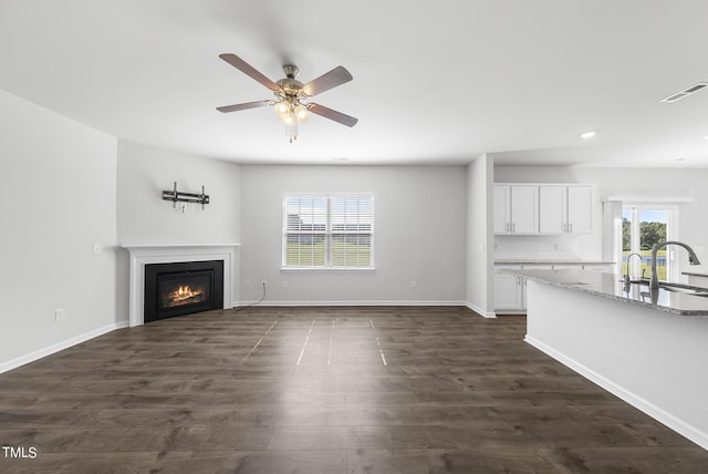 unfurnished living room with visible vents, dark wood-type flooring, baseboards, a warm lit fireplace, and a sink