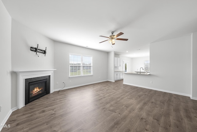 unfurnished living room featuring dark wood-style floors, a glass covered fireplace, baseboards, and a sink