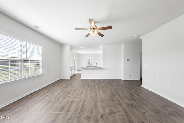 unfurnished living room with ceiling fan, baseboards, dark wood-style floors, and a sink