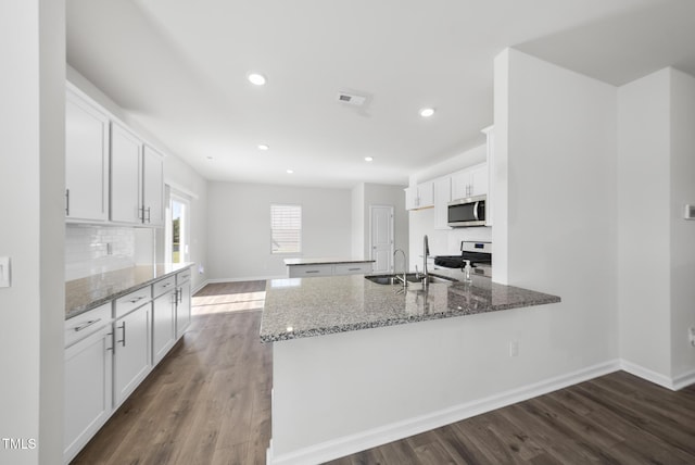 kitchen with light stone counters, dark wood finished floors, a peninsula, appliances with stainless steel finishes, and white cabinetry