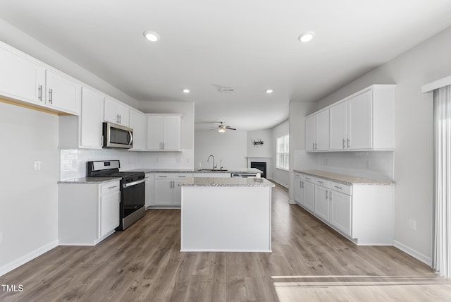 kitchen featuring light stone counters, decorative backsplash, appliances with stainless steel finishes, a ceiling fan, and a sink