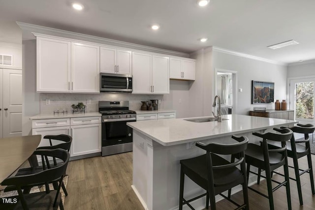 kitchen with sink, white cabinetry, crown molding, appliances with stainless steel finishes, and a kitchen island with sink