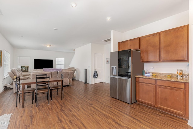 kitchen with dark wood-type flooring, light stone counters, and stainless steel fridge with ice dispenser