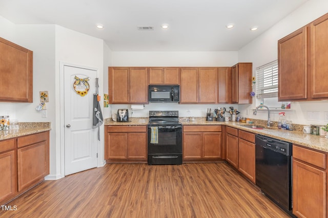 kitchen with dark wood-type flooring, sink, light stone counters, and black appliances