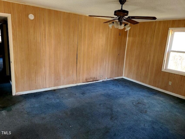 empty room featuring ceiling fan, wooden walls, a textured ceiling, and dark colored carpet