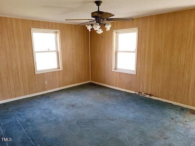 empty room with ceiling fan, plenty of natural light, a textured ceiling, and dark colored carpet