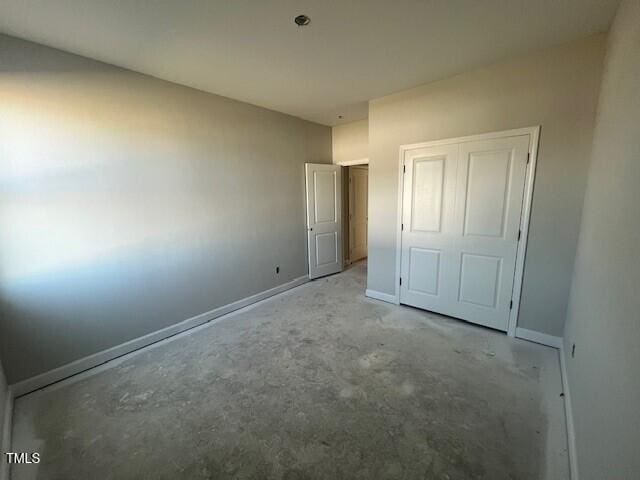 unfurnished bedroom with concrete floors, a closet, and baseboards