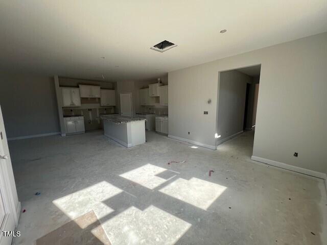 interior space featuring open floor plan, a kitchen island, white cabinetry, and baseboards