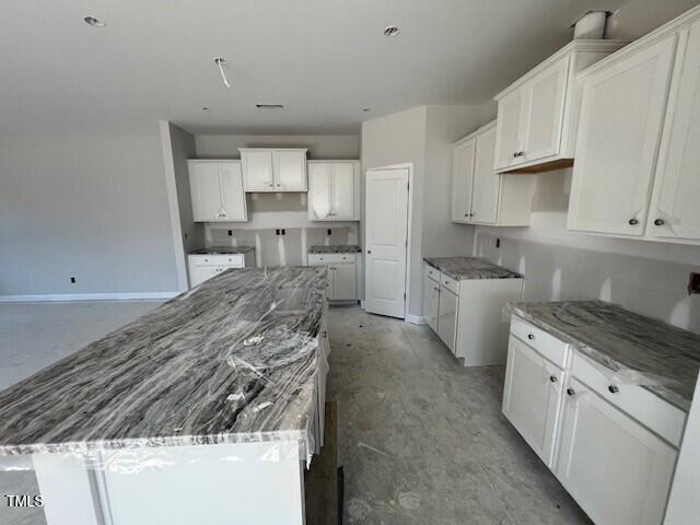 kitchen with stone counters, baseboards, white cabinetry, and a center island