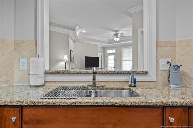 kitchen featuring light stone counters, ceiling fan, crown molding, and sink