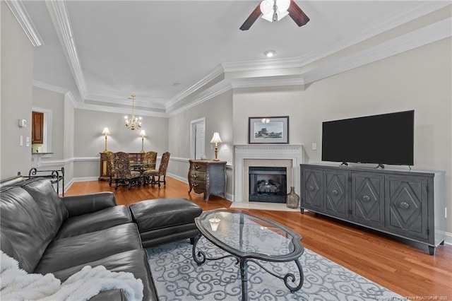 living room with hardwood / wood-style flooring, crown molding, ceiling fan with notable chandelier, and a tray ceiling