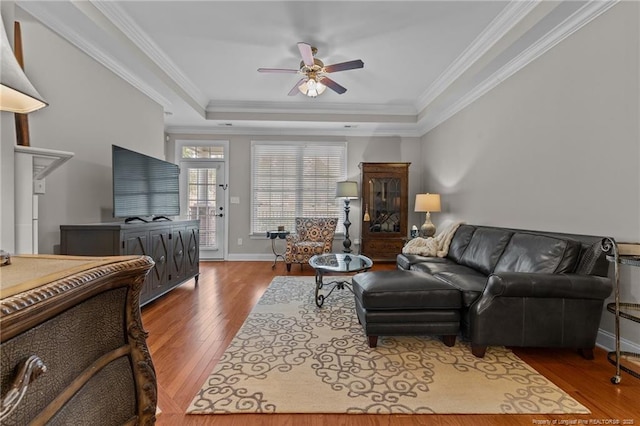 living room with a raised ceiling, ornamental molding, hardwood / wood-style floors, and ceiling fan