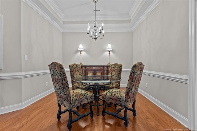 dining room with a raised ceiling, wood-type flooring, a notable chandelier, and crown molding