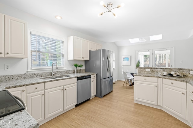 kitchen with white cabinets, appliances with stainless steel finishes, light stone countertops, light wood-style floors, and a sink