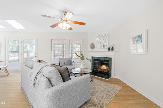 living area featuring ceiling fan, a premium fireplace, a skylight, baseboards, and light wood-style floors