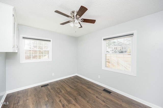 unfurnished room with a wealth of natural light, a textured ceiling, and dark hardwood / wood-style flooring