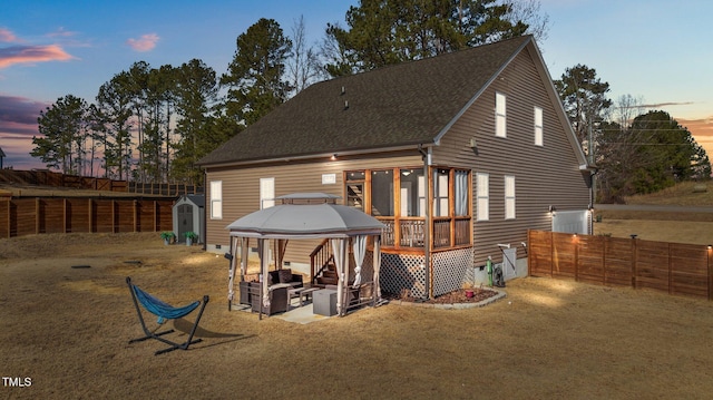 back house at dusk featuring a gazebo, central AC, a sunroom, and a lawn