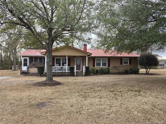 ranch-style house featuring covered porch, a chimney, metal roof, and a front yard