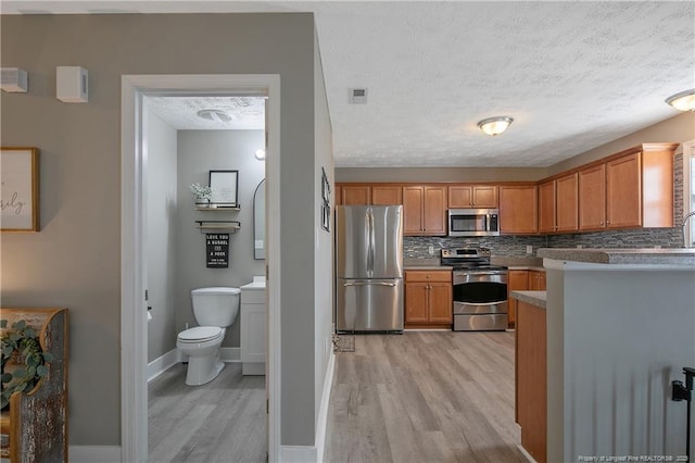 kitchen featuring appliances with stainless steel finishes, light wood-type flooring, a textured ceiling, and backsplash