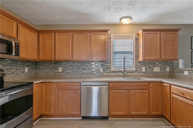 kitchen with sink, tasteful backsplash, light hardwood / wood-style flooring, a textured ceiling, and stainless steel appliances