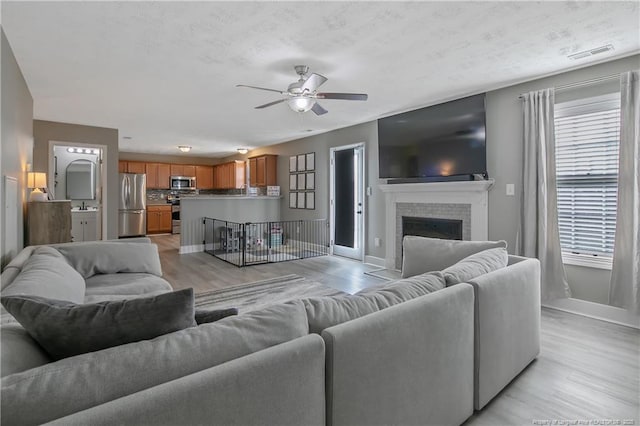 living room with ceiling fan, a fireplace, and light hardwood / wood-style floors