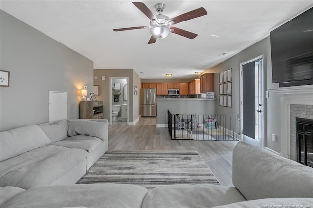 living room featuring ceiling fan, a fireplace, and light wood-type flooring