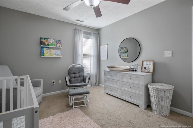 bedroom with a textured ceiling, light colored carpet, a nursery area, and ceiling fan