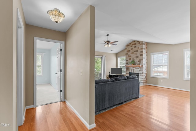 living room featuring vaulted ceiling, ceiling fan, a fireplace, and light hardwood / wood-style floors