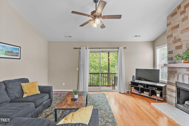 living room featuring hardwood / wood-style floors, a stone fireplace, plenty of natural light, and vaulted ceiling