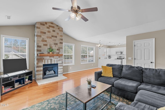 living room with lofted ceiling, ceiling fan with notable chandelier, rail lighting, light hardwood / wood-style floors, and a stone fireplace