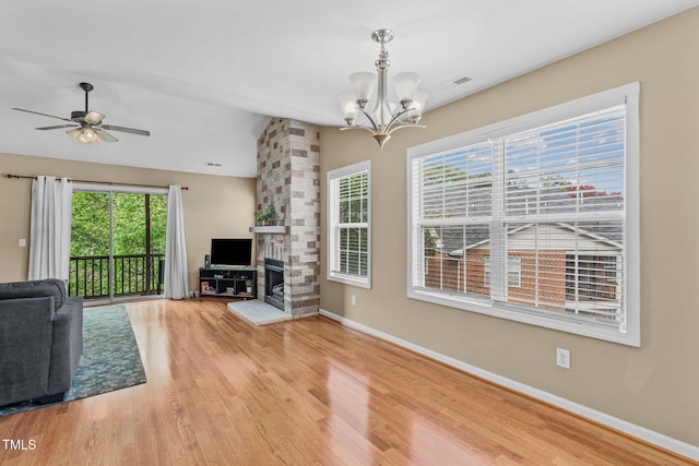 unfurnished living room featuring hardwood / wood-style floors, a stone fireplace, vaulted ceiling, and ceiling fan with notable chandelier