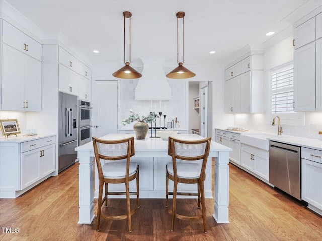 kitchen with white cabinetry, hanging light fixtures, custom range hood, and appliances with stainless steel finishes