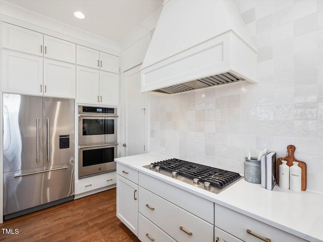 kitchen with white cabinetry, stainless steel appliances, dark hardwood / wood-style floors, tasteful backsplash, and custom exhaust hood