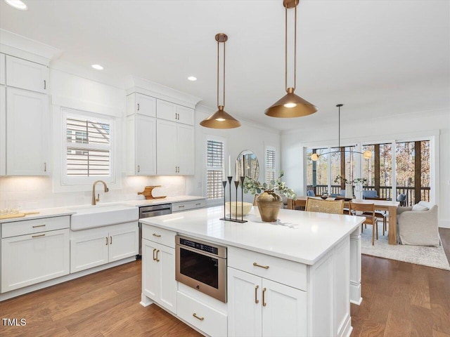 kitchen featuring decorative light fixtures, white cabinetry, sink, backsplash, and stainless steel oven