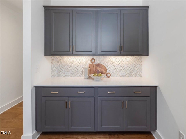 bar with gray cabinetry, decorative backsplash, and dark hardwood / wood-style flooring