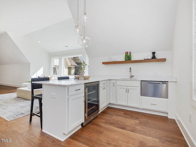 kitchen with decorative light fixtures, sink, white cabinets, beverage cooler, and kitchen peninsula